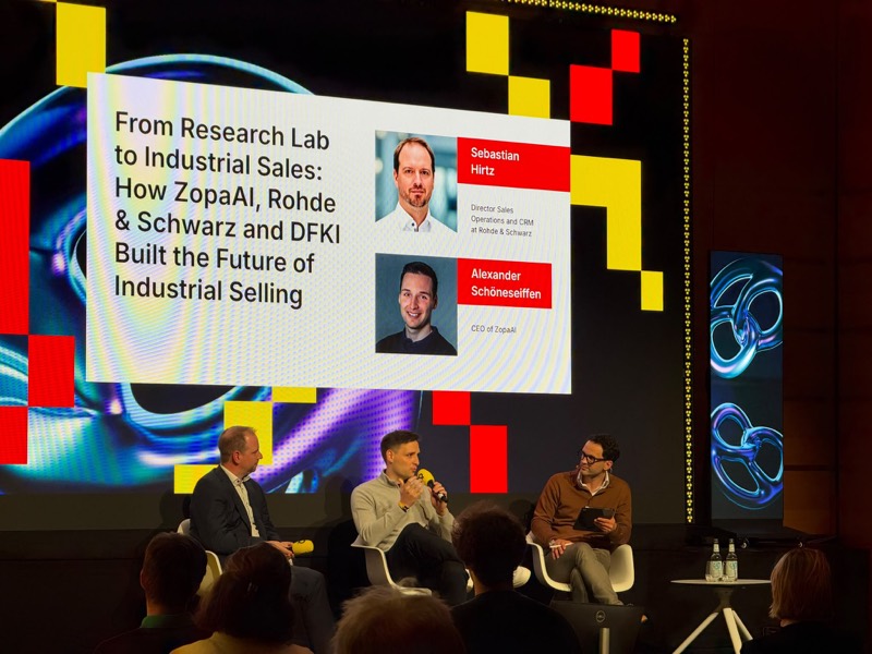 Podiumsdiskussion auf der Bühne der Bits & Pretzels 2026, unter einer Folie mit dem Titel „From Research Lab to Industrial Sales: How ZopaAI, Rohde & Schwarz and DFKI Built the Future of Industrial Selling“.